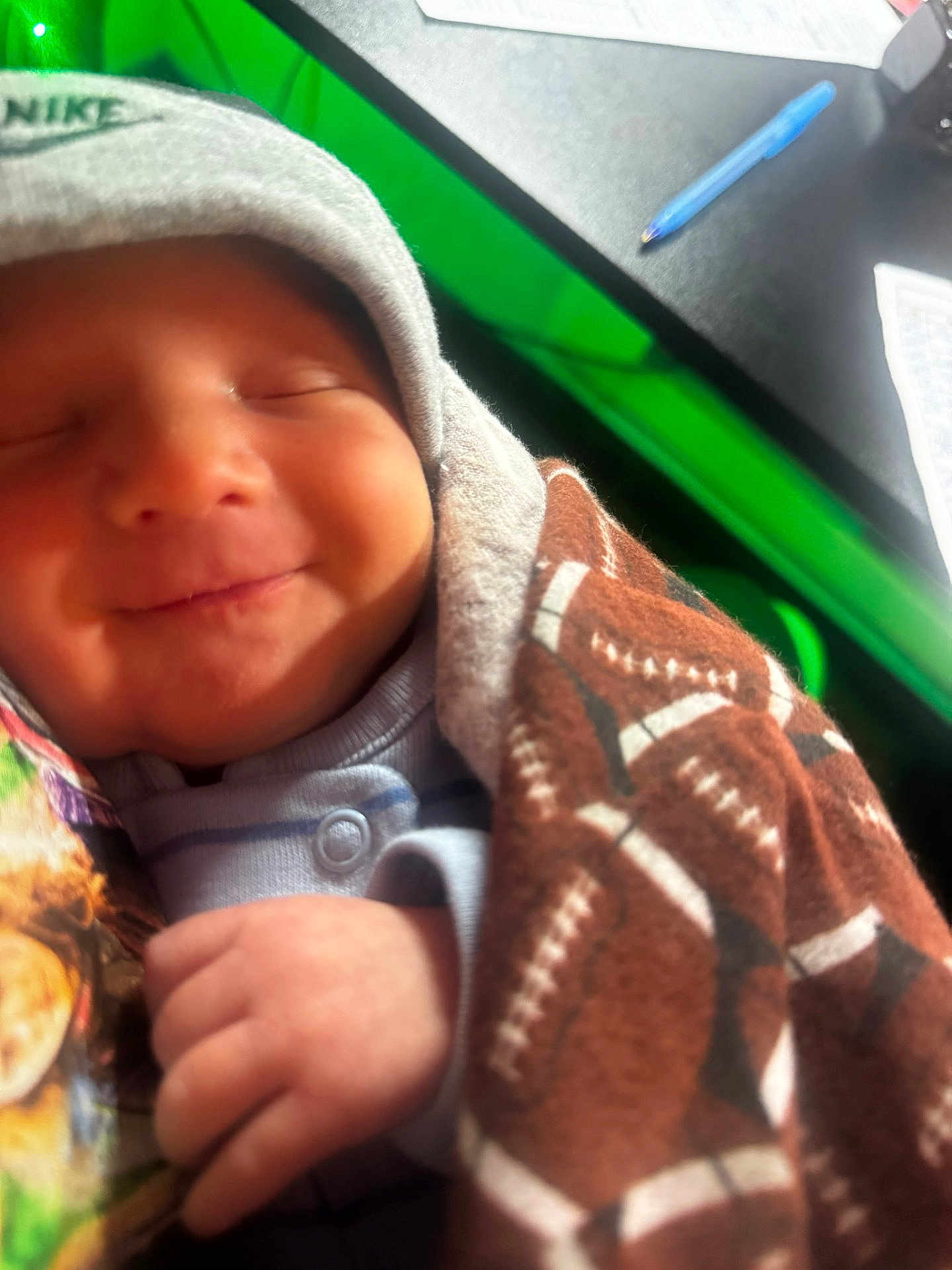 Brolee joined the competition — help win amazing prizes! baby, smiling, face, hood, blanket, football_pattern, hand, clothing, newborn, peaceful, indoor, desk, pen, paper, closeup, soft, wrapped, child, person, cozy