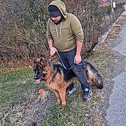 Aïka participe au concours pour gagner de l'argent avec cette photo : man, dog, german_shepherd, leash, hoodie, beanie, grass, bushes, road, sidewalk, outdoor, nature, pet, animal, walking, casual_clothing, shoes, happy, tongue_out, cool_weather