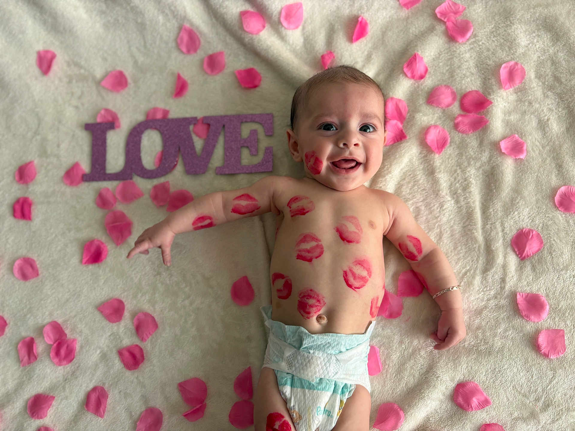 Giovanni is registered to the contest to win money with this photo: baby, infant, child, diaper, lipstick_marks, kiss_marks, pink_petals, love_sign, blanket, smiling, happy, face, eyes, arm, bracelet, lying_down, portrait, soft_texture, cute, closeup