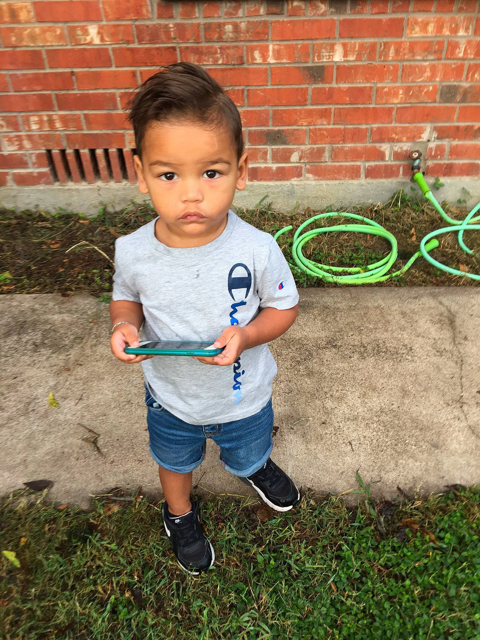 Renzo is registered to the contest to win money with this photo: baby_toddler_clothing, brick, brickwork, child, cool, fun, grass, happy, head, leaf, leisure, nature, people_in_nature, person, plant, public_space, shorts, standing, t_shirt, toddler