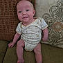 baby, infant, onesie, couch, pillow, home, furniture, smile, face, sitting, child, cute, pattern, textile, skin, legs, arms, indoors, person, comfortable
