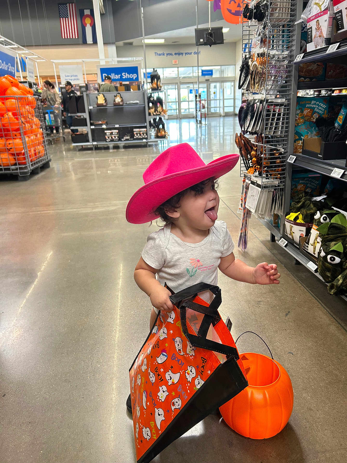Maeve joined the competition — help win amazing prizes! toddler, child, pink_hat, cowboy_hat, halloween, pumpkin_bucket, shopping_bag, store_interior, aisle, toys, decorations, floor, smiling, playful, curly_hair, clothing, retail, holiday, fun, person