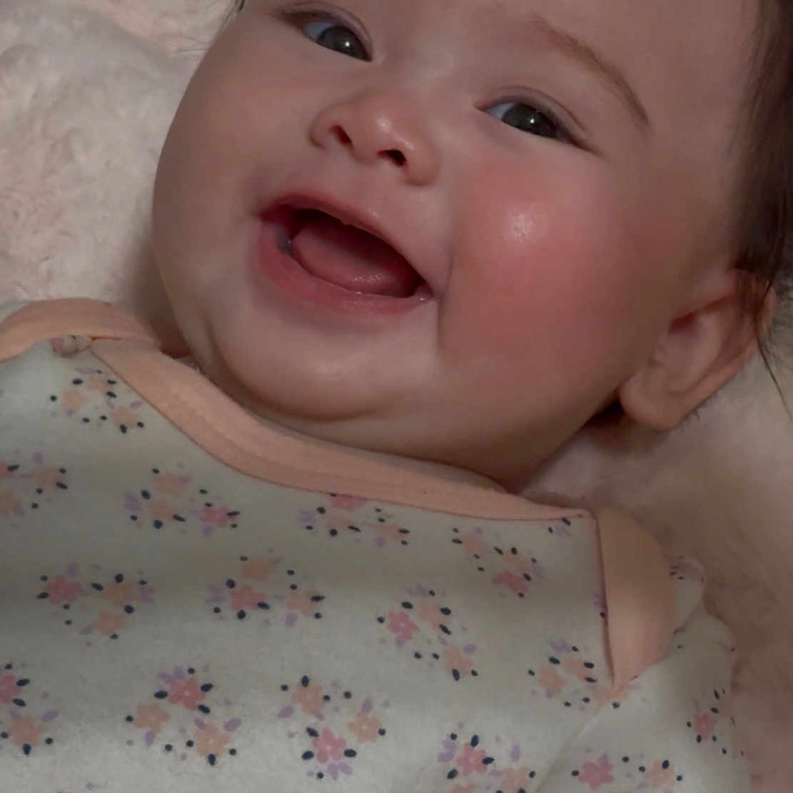 Mariko is registered to the contest to win money with this photo: baby, cheeks, child, clothing, cute, expression, eyes, face, floral_pattern, hair, happy, head, infant, lying_down, mouth, onesie, skin, smile, soft_texture, tongue