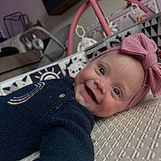Elena joined the competition — help win amazing prizes! baby, smiling, headband, bow, blue_sweater, infant, lying_down, play_area, indoor, toy, patterned_surface, face, happy, child, closeup, cute, person, home, soft_lighting, portrait