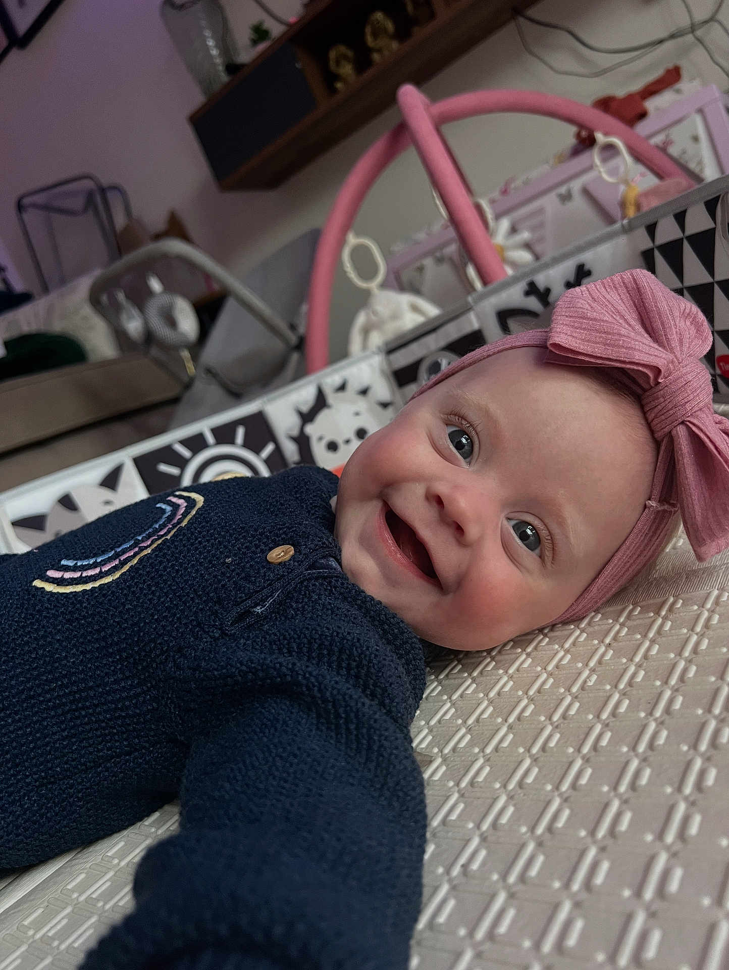 Elena joined the competition — help win amazing prizes! baby, smiling, headband, bow, blue_sweater, infant, lying_down, play_area, indoor, toy, patterned_surface, face, happy, child, closeup, cute, person, home, soft_lighting, portrait