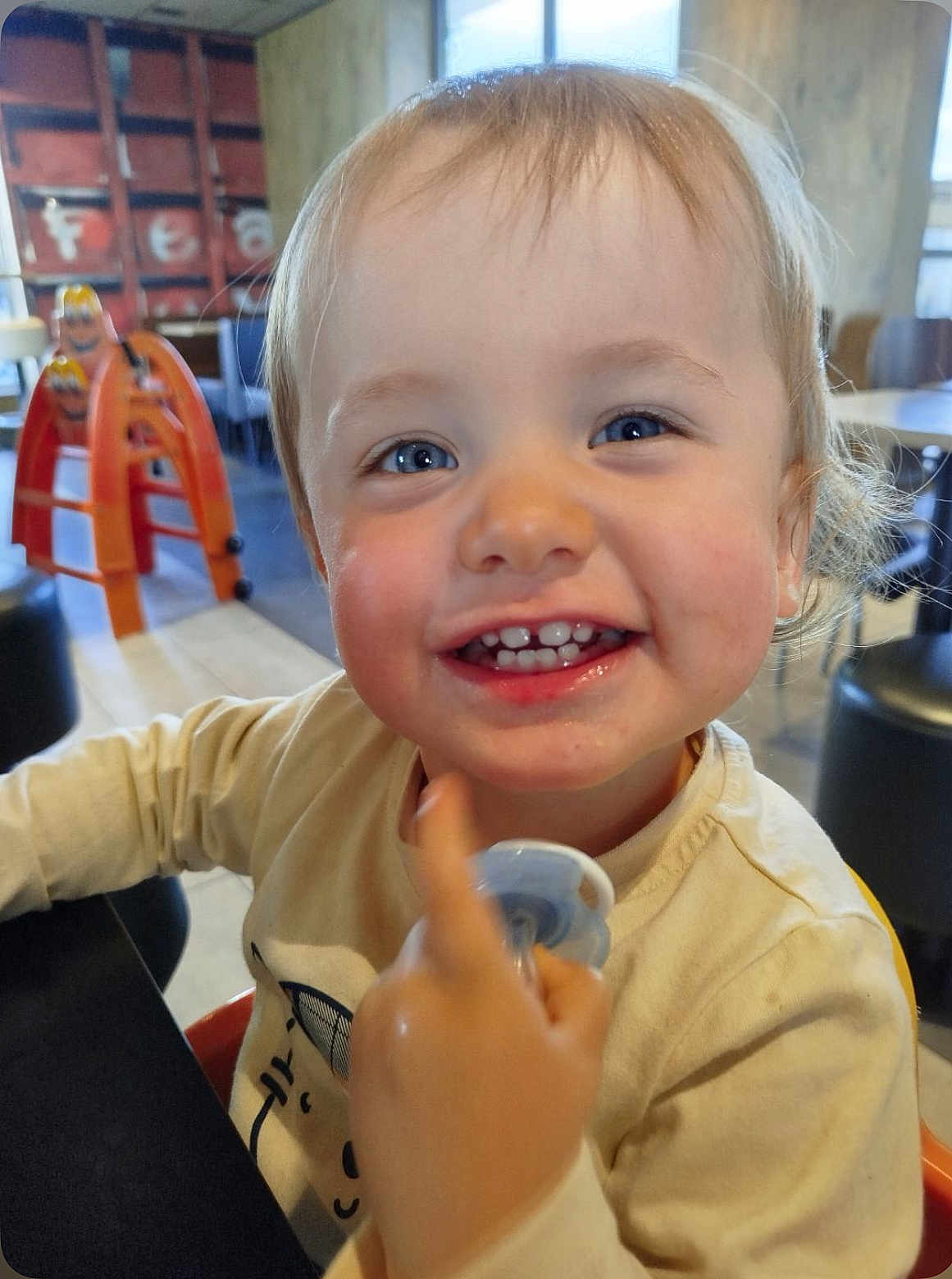 Milann participe au concours pour gagner de l'argent avec cette photo : toddler, child, smile, happy, face, blue_eyes, indoor, pacifier, pointing, blond_hair, long_sleeve, table, chair, furniture, playroom, cute, person, portrait, baby, expression