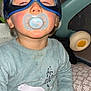 child, baby, pacifier, mask, captain_america, blue_outfit, polar_bear, toy, baby_gear, hand, face, indoor, cute, sleepy, messy, clothing, person, sitting, infant, hooded_mask