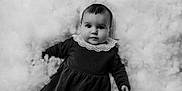 Emy participe au concours pour gagner de l'argent avec cette photo : baby, child, portrait, black_and_white, dress, lace_collar, face, eyes, hand, fluffy_background, soft_texture, cute, infant, lying_down, monochrome, young, person, studio, innocence, calm