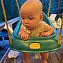 Koen is registered to the contest to win money with this photo: baby, child, swing, outdoor, porch, evening, curious, teal, plastic, wooden_floor, ropes, face, hands, feet, clothing, seat, furniture, lights, expression, person