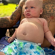Koen is registered to the contest to win money with this photo: baby, child, tattoo, adult, outdoor, sunlight, shorts, drool, skin, lap, person, portrait, summer, relaxing, bare_chest, blue, green, pattern, casual, expression