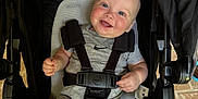 Koen is registered to the contest to win money with this photo: baby, child, smile, stroller, seatbelt, infant, happy, blue_eyes, rosy_cheeks, grey_outfit, sitting, indoor, person, cute, baby_clothing, head, legs, hands, comfort, straps