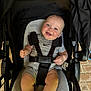 baby, child, smile, stroller, seatbelt, infant, happy, blue_eyes, rosy_cheeks, grey_outfit, sitting, indoor, person, cute, baby_clothing, head, legs, hands, comfort, straps