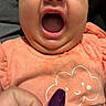 baby, infant, child, portrait, close_up, face, smiling, laughing, open_mouth, happy, eyes, peach_clothing, onesie, gingerbread, hearts, hand, fingernail, purple_nail_polish, indoor, couch