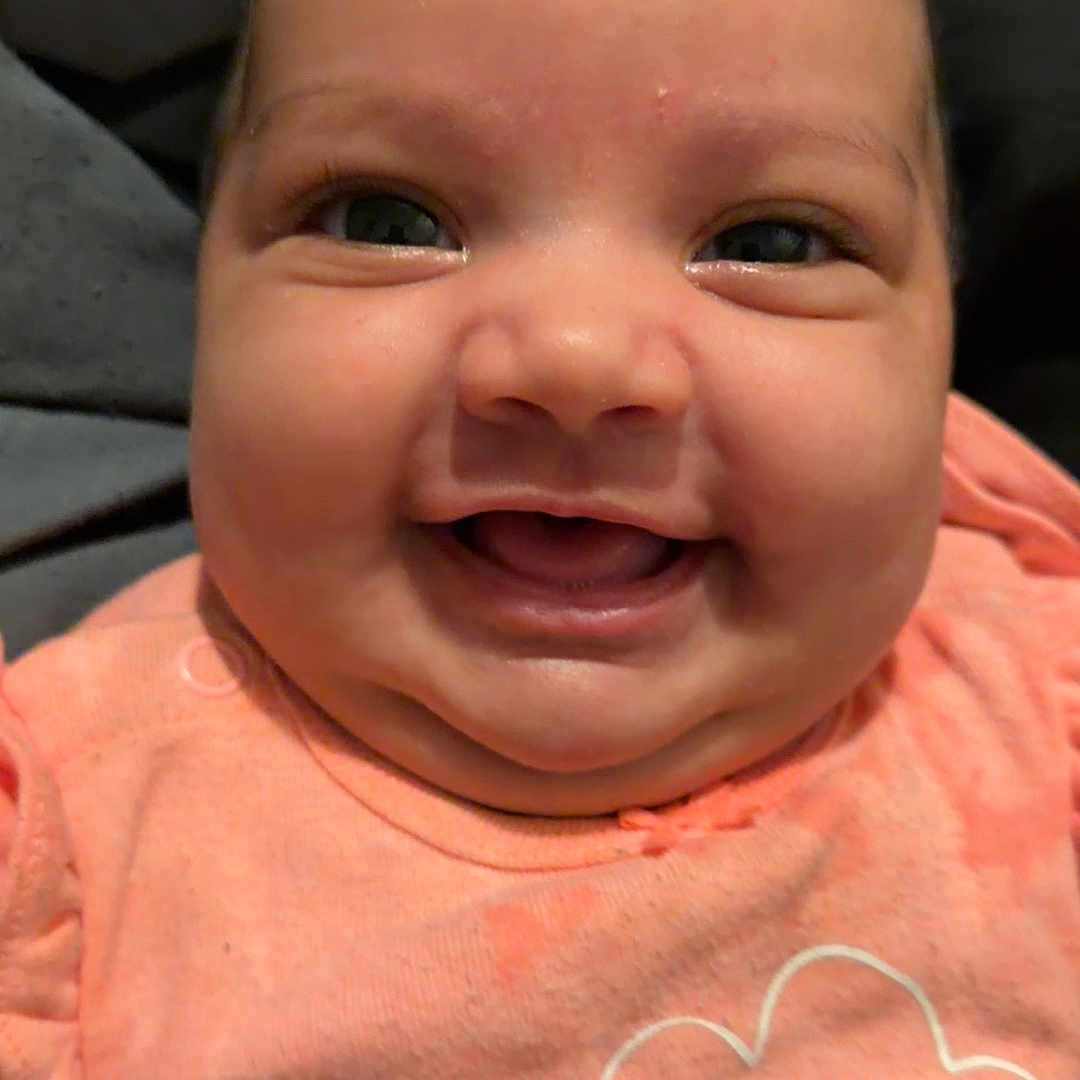 Amiyah Renee is registered to the contest to win money with this photo: baby, infant, child, smiling, happy, portrait, close_up, face, eyes, cheeks, mouth, peach_clothing, cloud_design, indoor, bedding, cuddly, adorable, sitting, headshot, photography