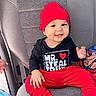 baby, black_shirt, blanket, car_seat, child, clothing, cute, face, hand, happy, infant, interior, person, portrait, red_hat, red_pants, seat, sitting, smiling, text_on_clothing