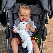 Maddy participe au concours pour gagner de l'argent avec cette photo : baby, child, cute, expression, footwear, happy, outdoor, person, pigtails, playful, plush_toy, seatbelt, shirt, shorts, sidewalk, stroller, summer_clothing, toddler, toy, white_toy
