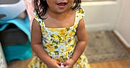 Maricela is registered to the contest to win money with this photo: child, girl, dress, yellow, hair_bows, purse, indoor, floor, wooden_floor, smile, face, person, young_child, curly_hair, cute, fashion, portrait, standing, home, happy