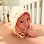 baby, infant, bonnet, tummy_time, cute, child, portrait, soft_lighting, indoor, crib, bed, skin, hand, face, wide_eyes, peach, fabric, headwear, resting, curious