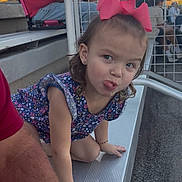 Mylah joined the competition — help win amazing prizes! child, girl, pink_bow, tongue_out, bleachers, metal, bracelet, earrings, short_sleeve, floral_dress, playful, outdoor, people, fence, crowd, casual_clothing, daylight, portrait, expression, kneeling
