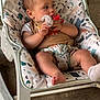 baby, infant, child, pacifier, baby_rocker, patterned_fabric, clothing, socks, seat, indoor, floor, toy, hand, face, head, legs, barefoot, comfort, relaxing, casual