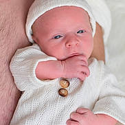 Liam a rejoint le concours — aidez-le/la à gagner de superbes lots ! newborn, baby, infant, white_clothing, knit_hat, knit_sweater, hand, fingers, resting, adult_arm, tattoo, skin, closeup, portrait, sleepy, cute, soft_light, indoor, cozy, peaceful
