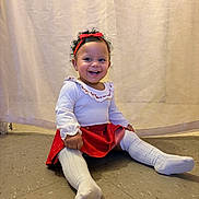 Zariah joined the competition — help win amazing prizes! child, clothing, curly_hair, curtain, cute, floor, happy, headband, indoor, long_sleeve, person, portrait, red_bow, red_skirt, sitting, smiling, toddler, white_socks, white_top, young_child