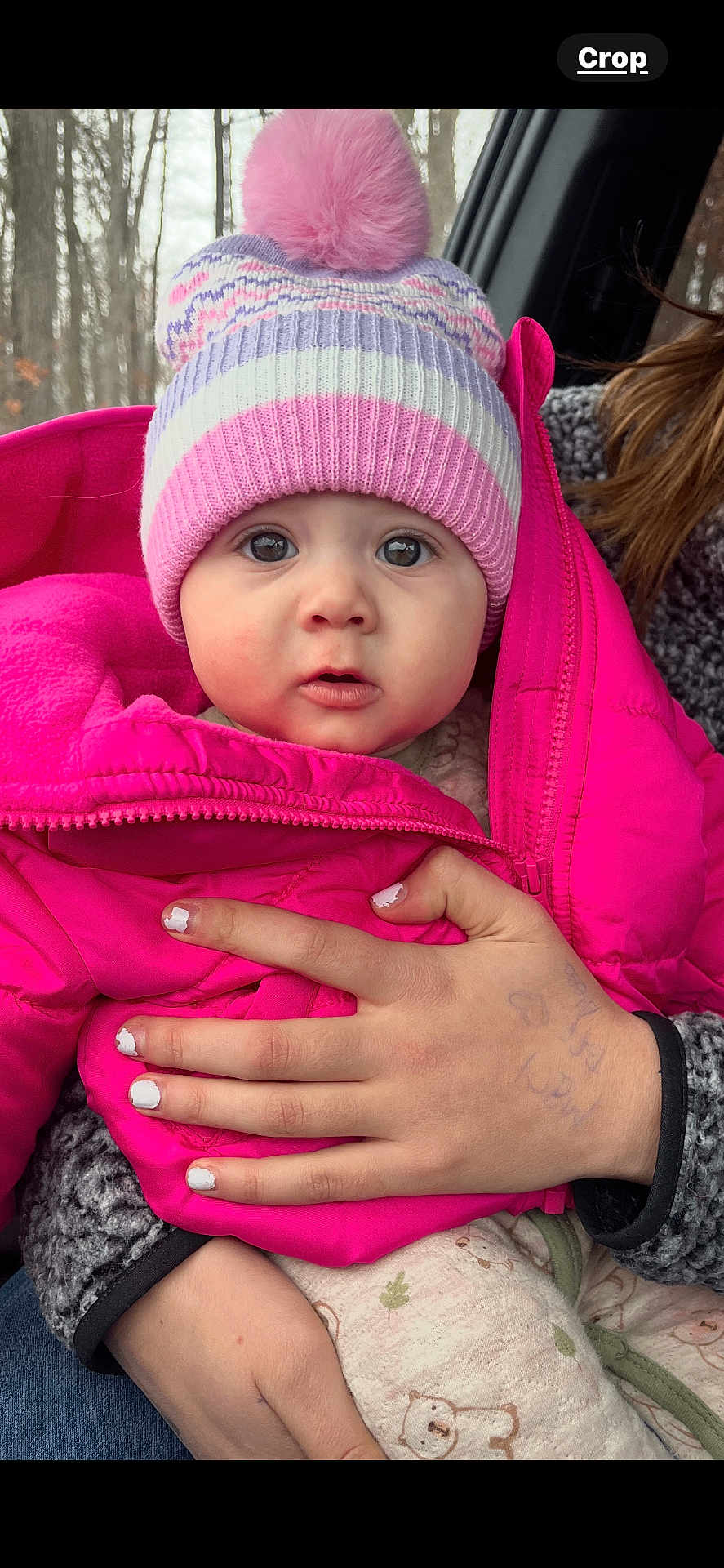Rori is registered to the contest to win money with this photo: baby, child, hat, pink_jacket, pom_pom, hand, nail_polish, pen_marks, forest, car_interior, winter_clothing, cozy, cute, portrait, outdoor_background, warm_clothes, infant, person, face, expression