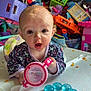 baby, high_chair, toy, food_smudge, child, indoor, messy_background, colorful, plastic_toys, teething_ring, face, clothing, curious, table, playroom, childhood, young_child, person, infant, expression