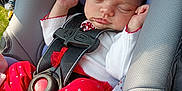 Theresia is registered to the contest to win money with this photo: baby, car_seat, child, cute, fabric, face, hand, indoors, infant, newborn, peaceful, red_pants, resting, safety, seatbelt, sleeping, transport, warning_label, white_shirt, young_child