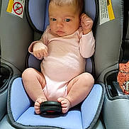 Theresia is registered to the contest to win money with this photo: baby, black_object, blue_padding, car_seat, child, curious, face, feet, grey_padding, hands, head, indoor, infant, newborn, padded_seat, pink_onesie, relaxed, seated, soft_lighting, warning_label