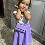 child, girl, posing, purple_skirt, white_top, purse, marble_wall, floor, sandals, smiling, cute, standing, indoors, fashion, accessories, portrait, person, young, happy, playful