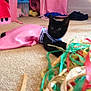 Josephine joined the competition — help win amazing prizes! black_cat, kitten, carpet, pink_cloth, colorful_ribbons, indoor, pet, animal, toy, floor, curious, furniture, cloth, decor, playful, small_animal, cute, domestic_cat, household, resting