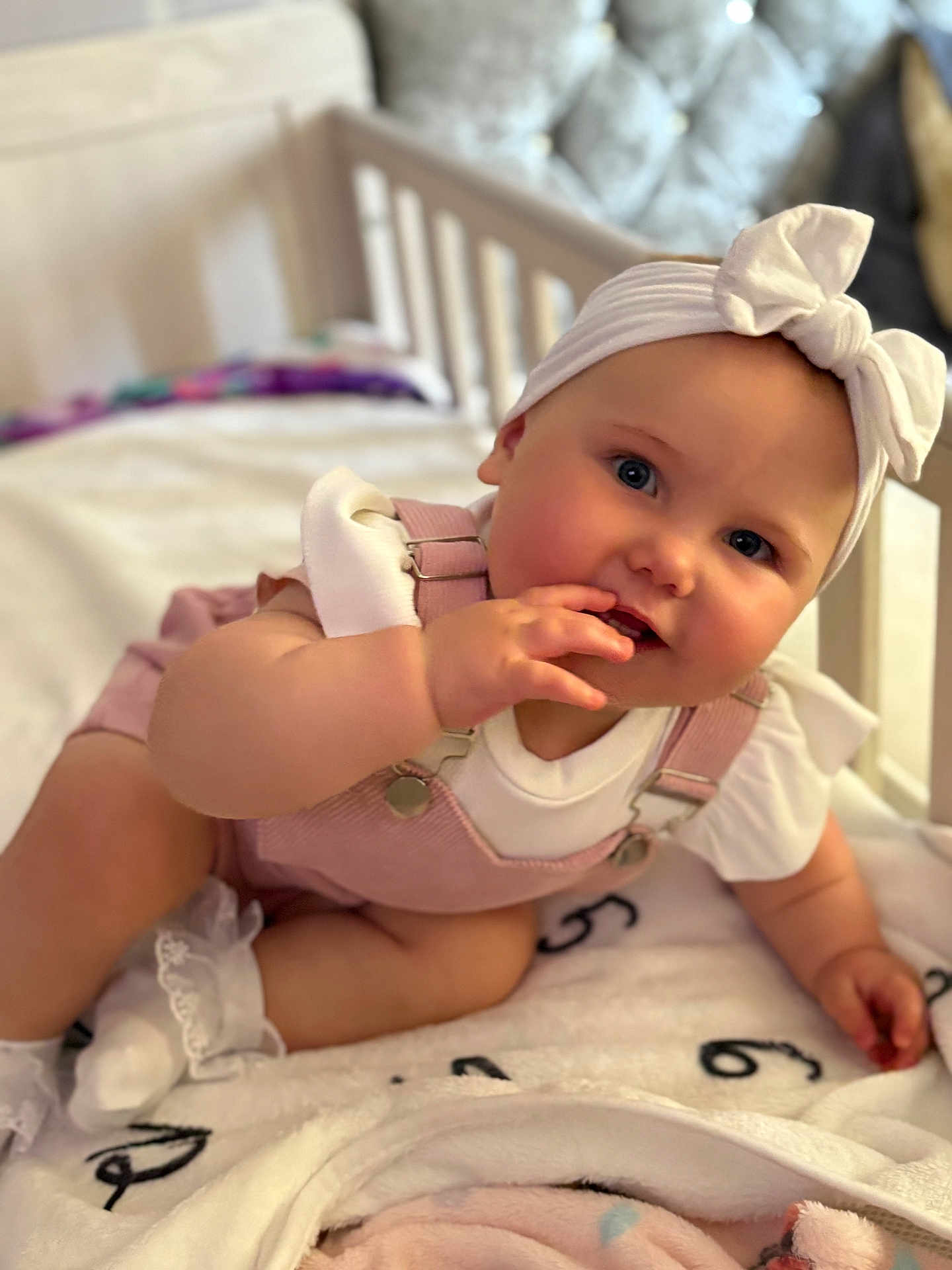 Olivia is registered to the contest to win money with this photo: baby, infant, child, face, headband, bow, overalls, pink, white, blanket, crib, furniture, cute, soft, sock, sitting, hand, cheeks, portrait, indoors