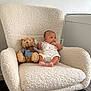baby, carpet, child, clothing, cozy, cute, decor, foot, furniture, indoor, infant, person, plush_toy, rocking_chair, room, sitting, soft_texture, teddy_bear, toy, white_wall