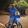 basket, bicycle, bush, canine, casual_clothing, dog, headlight, lamp_post, leisure, man, night, outdoor, person, pet, road, shadow, sidewalk, streetlight, tree, vehicle