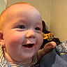 John-Michael is registered to the contest to win money with this photo: baby, smiling, face, cheeks, indoor, striped_clothing, person, child, happy, head, skin, blue_shirt, window, furniture, background, cute, infant, expression, leaning, young