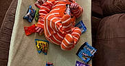 John-Michael is registered to the contest to win money with this photo: baby, child, candy, snickers, orange_pajamas, striped_clothing, blanket, couch, smiling, holding, wrapped_candy, lollipop, fun_size_candy, indoor, playful, cute, person, infant, lying_down, holiday
