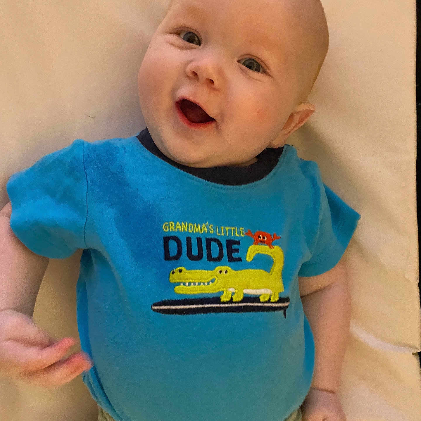 John-Michael joined the competition — help win amazing prizes! baby, blue_shirt, crocodile, cartoon, happy, infant, smiling, child, cute, lying_down, clothing, toddler, face, person, indoor, playful, expression, background, soft_surface, casual