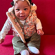 Eve is registered to the contest to win money with this photo: baby, bow, child, couch, cozy, curly_hair, cute, fashion, green_pants, happy, headband, indoor, person, portrait, red, sitting, smiling, socks, vest, white_shirt