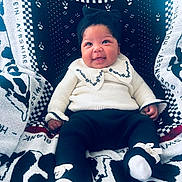 Eve joined the competition — help win amazing prizes! baby, smiling, knitted_clothing, hat, socks, blanket, patterned_blanket, seated, cute, portrait, indoors, infant, warm_clothing, bow, happy, child, face, person, cozy, closeup