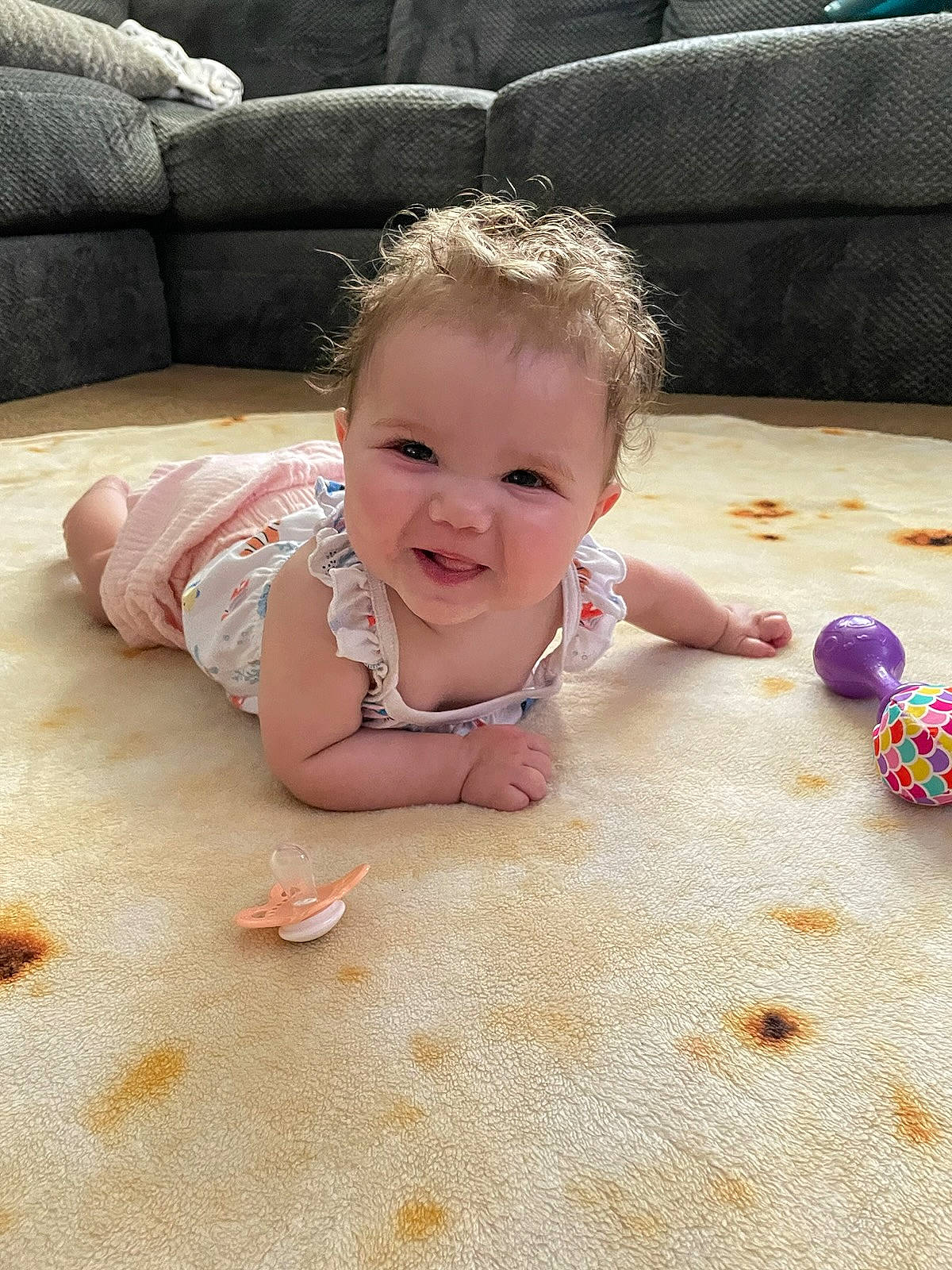 Ila is registered to the contest to win money with this photo: baby, baby_toddler_clothing, cheek, child, comfort, couch, face, facial_expression, floor, flooring, fun, grass, happy, head, person, pink, sitting, skin, smile, toddler