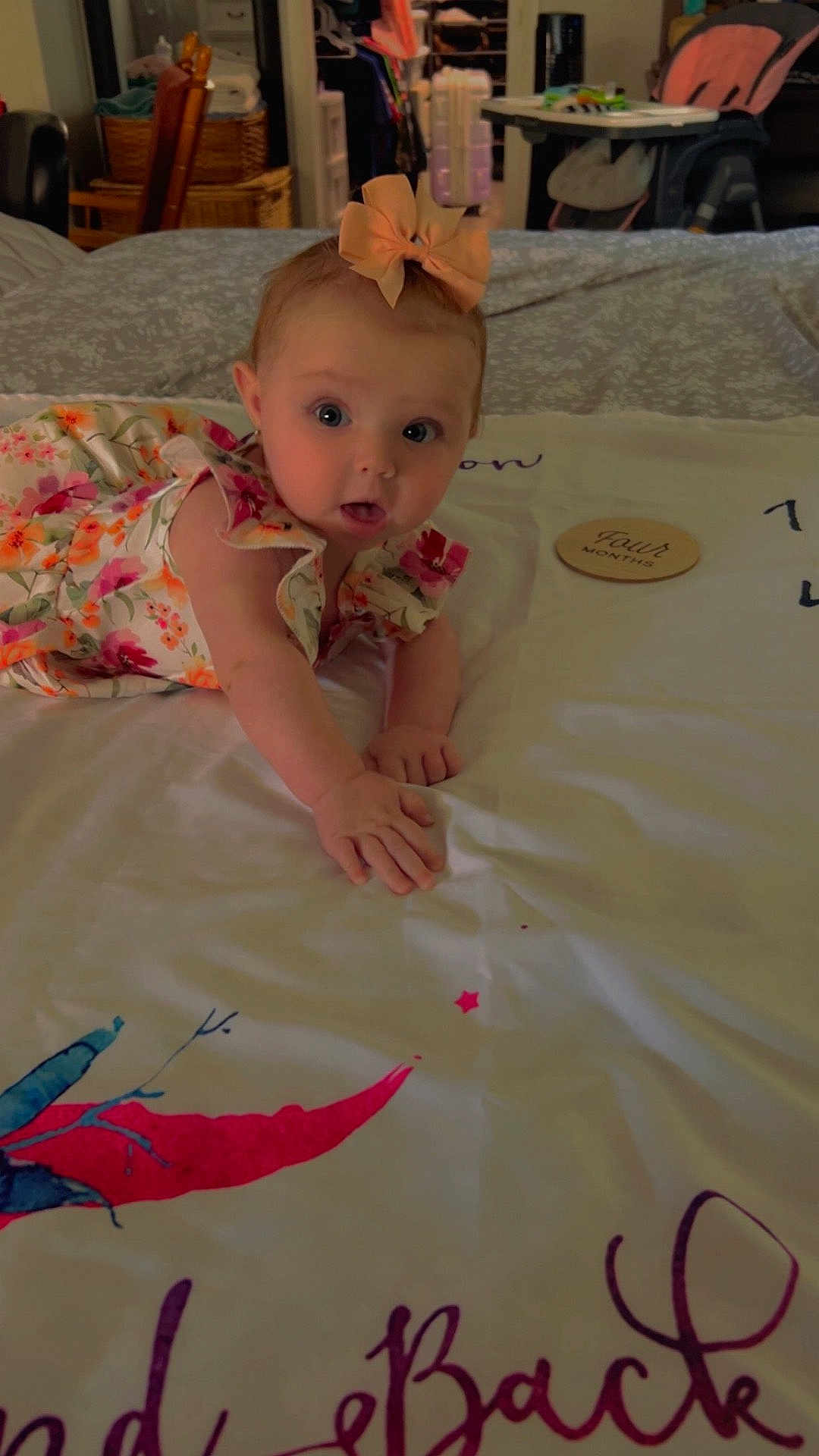 Emma joined the competition — help win amazing prizes! baby, child, girl, bow, floral_dress, tummy, bed, blanket, room, furniture, highchair, basket, curious, wide_eyes, indoor, soft_lighting, hand, head, person, cute
