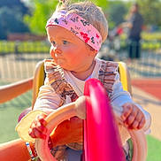 Léa a rejoint le concours — aidez-le/la à gagner de superbes lots ! blurred_background, butterfly, child, clothing, daylight, face, fun, hands, headband, outdoor, park, person, pink, playground, smile, steering_wheel, sunlight, support, toddler, young_child