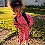 child, smiling, pink_tracksuit, backpack, outdoor, sunny, grass, tree, house, shoes, side_pose, happy, curly_hair, hair_bow, daylight, shadow, casual_clothing, young, person, playful