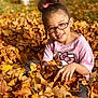 child, glasses, pink_shirt, hello_kitty, autumn_leaves, fall, outdoor, smiling, happy, girl, nature, seasonal, brown_leaves, yellow_leaves, hair_bun, sunlight, playful, casual_clothing, portrait, young