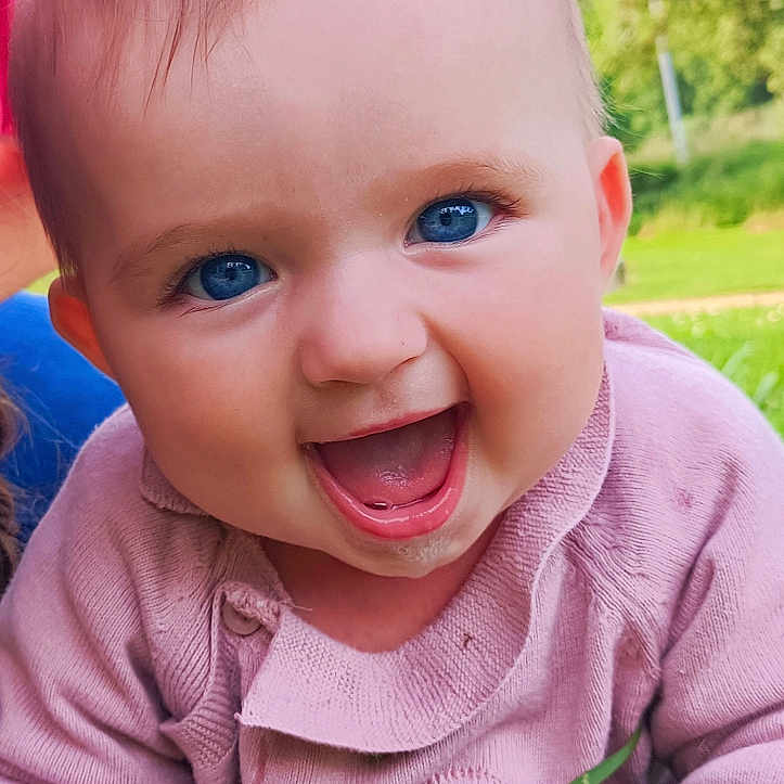 Théa a rejoint le concours — aidez-le/la à gagner de superbes lots ! baby, blue_eyes, child, closeup, crawling, cute, daytime, face, grass, greenery, happy, infant, joyful, nature, outdoor, pink_clothing, portrait, smiling, sunlight, young_child