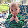 baby, child, toddler, portrait, sitting, eating, snack, food, crumbs, smiling, face, eyes, hands, striped_shirt, green_clothing, chair, outdoor, garden, patio, sunlight