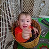 Aaron is registered to the contest to win money with this photo: toddler, child, baby, smiling, happy, portrait, indoor, basket, wicker, snack, food, orange_shirt, playpen, baby_gate, carpet, play_mat, toy_room, sitting, face, hand