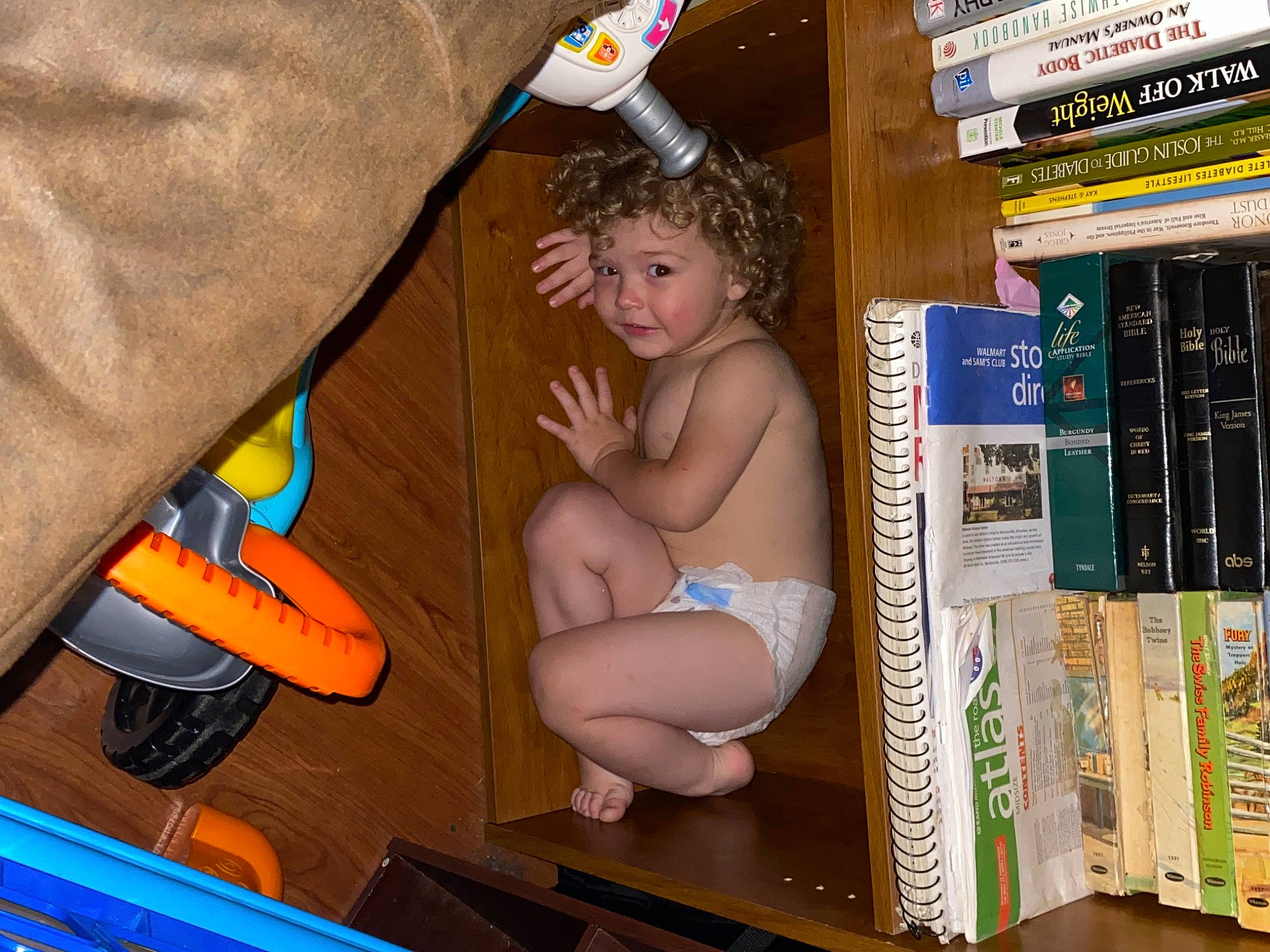 Declan is registered to the contest to win money with this photo: abdomen, barechested, barefoot, book, bookcase, chest, child, diaper, foot, fun, human_leg, knee, leisure, person, publication, room, shelf, shelving, sitting, thigh