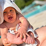 Noé a rejoint le concours — aidez-le/la à gagner de superbes lots ! baby, child, towel, hooded_towel, smiling, happy, barefoot, hand, foot, skin, outdoor, sunlight, poolside, blurred_background, person, cute, playful, infant, summer, portrait